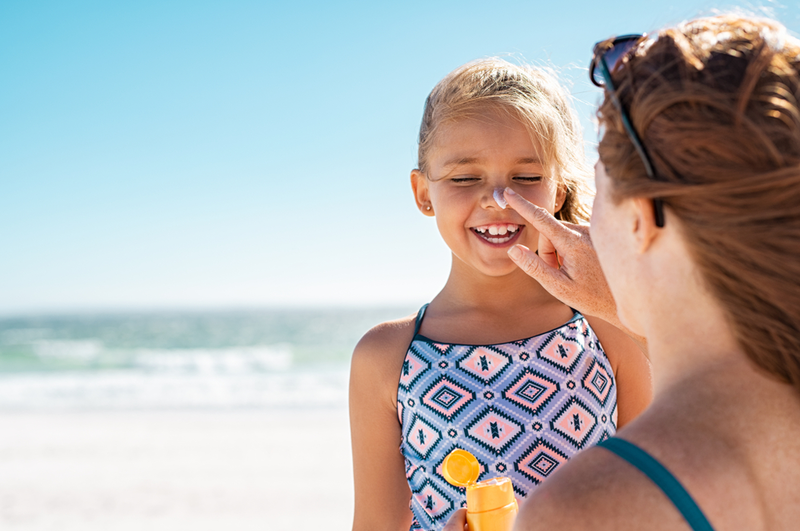 applying sunscreen on daughter's nose on the beach