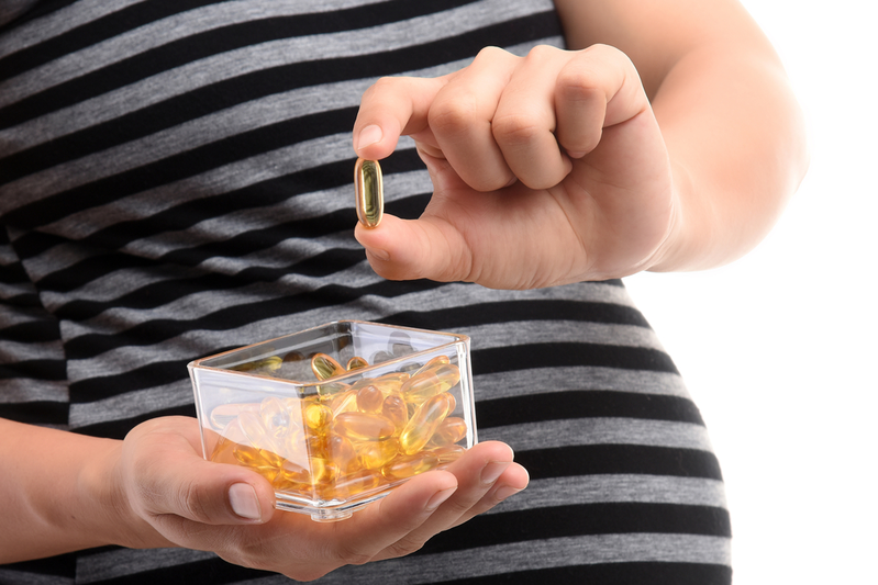 pregnant woman holding a fish oil supplement in front of stomach