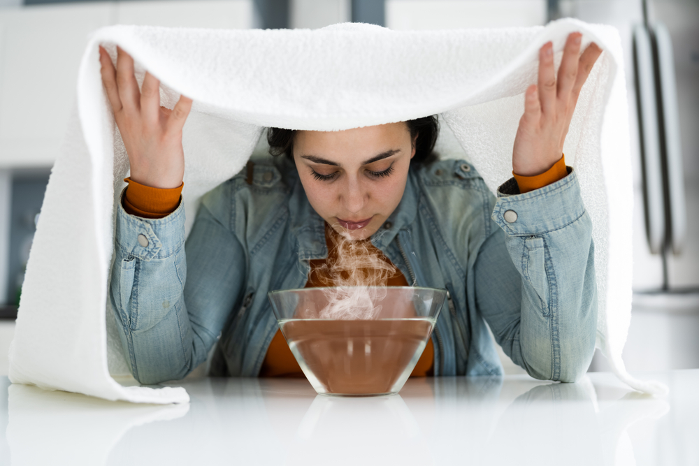 woman breathing in steam from bowl of hot water with towel overhead